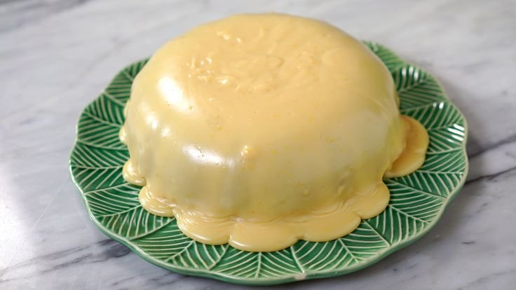 # Quando fiz esse bolo vulcão de laranja com brigadeiro branco cítrico, a conversa na sala simplesmente parou Meninas, preparem a vossa forma de cone central mais bonita e abram espaço na bancada porque a receita de hoje traz aquele monumento de confeitaria afetiva que faz qualquer um perder a postura no primeiro corte! Sabem aquele bolo vulcão alto, desenformado num prato verde de louça todo decorado, onde uma massa fofa, aerada e bem molhadinha de laranja natural fica completamente oculta sob um manto reluzente, acetinado e denso de brigadeiro branco cremoso com raspas cítricas, que escorre em cascatas aveludadas até formar ondas brilhantes na base? Pois bem, este bolo vulcão de laranja com brigadeiro branco cítrico é a definição exata de aconchego com requinte de vitrina gourmet. O segredo irresistível desta receita está no contraste: a doçura láctea do leite condensado ganha o equilíbrio perfeito com o suco fresco e o perfume dos óleos da casca da laranja, garantindo uma cobertura que envolve o bolo sem ficar enjoativa e que derrete na boca com maciez absoluta. Quero fazer um convite muito animado, carinhoso e cheio de energia a cada uma de vocês: vistam o vosso melhor avental, passem um café fresco no coador e venham comigo para a beira do fogão acompanhar este momento mágico! Poucas coisas na culinária caseira trazem tanta satisfação aos olhos do que preencher o centro do bolo morno com aquela calda aveludada e ver o brigadeiro transbordar como lava cremosa por cima de toda a crosta dourada até cobrir o bolo inteiro numa cúpula sedosa. Tenho a certeza absoluta de que, assim que colocarem este prato no centro da mesa com uma fatia farta a tombar no prato, toda a família vai esquecer as correrias e disputar quem fica com a colherada com mais cobertura. Venham daí aprender todas as dicas de mestre para acertar o ponto fluido do brigadeiro sem empelotar, não amargar as raspas e fazer um sucesso estrondoso com todo o mundo! ## Ingredientes do bolo vulcão de laranja com brigadeiro branco cítrico Para a massa fofinha, aerada e aromática: * 4 ovos médios inteiros biológicos em temperatura ambiente * 1 chávena e meia de açúcar refinado fino ou demerara (cerca de 270 g) * Meia chávena de óleo vegetal neutro de girassol ou milho (cerca de 120 ml, fundamental para a umidade que não resseca) * 2 colheres de sopa de manteiga sem sal em ponto de pomada (cerca de 40 g, confere sabor nobre e miolo sedoso) * 1 chávena de suco puro de laranja natural espremido e coado na hora (cerca de 240 ml, preferencialmente laranja-pera madura) * Raspas finas da casca de 2 laranjas (cuidado para retirar apenas a película colorida superficial sem tocar na parte branca) * 2 chávenas e meia de farinha de trigo sem fermento peneirada (cerca de 320 g) * Meia chávena de amido de milho peneirado (o toque secreto para a massa ficar levinha como pluma) * 1 colher de sopa bem cheia de fermento químico em pó para bolos * 1 pitadinha minúscula de sal marinho fino (para realçar as notas cítricas) Para a cobertura vulcânica de brigadeiro branco cítrico: * 2 latas ou caixinhas de leite condensado tradicional (790 g no total) * 2 caixinhas de natas ou creme de leite consistente (400 g) * 1 colher de sopa de manteiga sem sal de boa qualidade * Meia chávena de suco concentrado de laranja natural coado (cerca de 120 ml) * Raspas finas de 1 laranja-pera e de meio limão siciliano (para dar aquele perfume fresco e o pontilhado delicado na cobertura) * 1 colher de sopa de glucose de milho ou mel (opcional, garante brilho espelhado e textura de fita sedosa) Para preparar este espetáculo aveludado, utilizamos utensílios muito práticos presentes na cozinha de qualquer lar: uma forma redonda de alumínio polido com cone central (com cerca de 22 a 24 centímetros de diâmetro e bordas altas de pelo menos 8 cm), uma panela média e funda de fundo grosso para cozinhar o brigadeiro sem queimar as laterais, um ralador fino para as raspas cítricas, um espremedor de frutas, uma tigela ampla com batedor de arames (fouet) ou batedeira comum para emulsionar os ovos com açúcar, uma espátula de silicone resistente (pão-duro) e um prato de servir redondo com borda levantada (como a louça em relevo de folhas da foto) para conter todo o brigadeiro vulcânico que escorre com fartura. O tempo de dedicação ativa com as mãos na bancada é de cerca de 25 minutos entre bater a massa e apurar o brigadeiro no fogão, somando-se aproximadamente 40 a 45 minutos de forno a 180 graus e 10 minutos para amornar antes da montagem. A receita rende um bolo imponente de cerca de 12 a 14 fatias fartas, muito densas e pesadas de cobertura, perfeitas para coroar comemorações e cafés especiais com pura abundância. ## Modo de preparo da receita 1. Comece por pré-aquecer o forno a 180 graus. Unte a forma de cone central generosamente com manteiga e polvilhe com farinha de trigo em toda a base, paredes e tubo central, sacudindo o excesso sobre a pia. 2. Lave muito bem as laranjas sob água corrente. Com o ralador fino, retire as raspas perfumadas da casca de duas laranjas, tomando o cuidado de não atingir a entrecasca branca amarga. Esprema o suco e passe por uma peneira fina para eliminar bagaços e sementes. 3. Na tigela da batedeira (ou alguidar com a vara de arames), adicione os 4 ovos inteiros, o açúcar refinado peneirado e a pitadinha de sal marinho. Bata em velocidade média-alta durante cerca de 4 a 5 minutos até obter uma espuma clara, fofa, esbranquiçada e volumosa. 4. Adicione o óleo vegetal e as duas colheres de manteiga em ponto de pomada, batendo por mais 1 minuto até emulsionar os líquidos por completo. 5. Reduza a velocidade para o mínimo e adicione as raspas de casca de laranja. 6. Comece a acrescentar a farinha de trigo peneirada juntamente com o amido de milho aos poucos, intercalando com a chávena de suco de laranja natural em temperatura ambiente. Misture com a espátula de silicone em movimentos lentos de baixo para cima apenas até a farinha sumir, evitando bater em demasia para não ativar o glúten pesado. 7. Adicione a colher de fermento químico em pó por último, envolvendo suavemente de baixo para cima para distribuir a aeração de maneira uniforme. 8. Despeje a massa cremosa dentro da forma untada, batendo levemente o fundo da forma contra a bancada uma vez para assentar. 9. Leve ao forno pré-aquecido a 180 graus durante cerca de 40 a 45 minutos. O bolo estará pronto quando apresentar uma superfície dourada uniforme e, ao espetar um palito no centro, ele sair completamente seco e limpo. 10. Retire a forma do forno com luvas térmicas e deixe amornar na bancada por cerca de 15 minutos. Passe uma faquinha de ponta redonda delicadamente nas laterais e ao redor do cone central e desenforme o bolo morno no centro do prato de servir com borda alta. 11. Enquanto o bolo amorna, prepare a cobertura de brigadeiro branco cítrico: numa panela média de fundo grosso fora do fogo, junte as 2 latas de leite condensado, as 2 caixinhas de natas, a colher de manteiga sem sal e a glucose (se for usar). Misture com a espátula até ficar uniforme. 12. Leve a panela ao fogo médio-baixo, mexendo continuamente com a espátula pelo fundo e cantos da panela sem parar. 13. Quando o brigadeiro levantar fervura com borbulhas densas, continue mexendo por cerca de 6 a 8 minutos até engrossar num ponto de creme aveludado e encorpado (ponto de brigadeiro mole/fita fluida, antes do ponto de enrolar). 14. Desligue a chama do fogão. Imediatamente com o fogo desligado, despeje a meia chávena de suco concentrado de laranja e as raspas cítricas de laranja e limão siciliano. Misture vigorosamente com o fouet até que o suco se incorpore por completo. O ácido do suco em contato com o creme quente fora do fogo confere um brilho acetinado e uma consistência aveludada sem talhar o leite condensado. 15. Deixe o brigadeiro repousar por 5 minutos até ficar morno e sedoso. 16. Agora vem o grande espetáculo: verta o brigadeiro branco cítrico ainda morno diretamente dentro do furo central do bolo até que ele se encha completamente. Continue despejando sem pressa no centro até que o creme transborde em cascata contínua sobre as laterais, espalhando suavemente com as costas de uma colher para forrar toda a cúpula do bolo e formar aquela borda ondulada reluzente no prato que aparece na foto! 17. Deixe a cobertura assentar por 15 minutos em temperatura ambiente e sirva em fatias fartas, cortando com uma faca grande e puxando fatias onde a calda escorre em abundância pelo prato de sobremesa! No último domingo à tarde, decidi preparar este bolo vulcão com brigadeiro cítrico para o café em família e deixei o bolo a amornar no centro do meu prato verde favorito enquanto terminava de mexer o brigadeiro branco no fogão. O meu marido estava na sala compenetrado a tentar colar a aba quebrada de um controle de videogame com cola instantânea e dizia em tom muito sério que estava completamente focado no conserto e que nem ia olhar para a mesa porque tinha prometido a si mesmo cortar doces no fim de semana. Pois bem, bastou eu despejar aquela panela de brigadeiro branco no cone central e ver o creme reluzente transbordar em ondas perfeitas, cobrindo o bolo inteiro sob aquele aroma inebriante de calda quente de leite condensado com raspas de laranja fresca, para o controle de videogame bater direto no braço do sofá! Meninas, a conversa na sala simplesmente parou. O homem levantou-se num impulso, entrou na copa com os olhos fixos naquela cúpula brilhante que parecia uma joia de confeitaria e nem esperou que eu buscasse as xícaras! Ele puxou a faca de bolo, cortou a primeira fatia triangular e, assim que o miolo macio cedeu e o vulcão de brigadeiro desceu em cascata fumegante sobre a travessa, ele soltou um suspiro de pura glória! Deu uma garfada monumental de olhos semicerrados, ficou em silêncio absoluto por quase um minuto mastigando com um sorriso de ponta a ponta e disse com a cara mais lavada deste mundo que videogame funcionava quebrado, mas que um bolo de laranja com brigadeiro daquele calibre era patrimônio sagrado da família e que deixar de comer duas fatias gigantescas seria um atentado imperdoável contra a felicidade da casa! ## Acompanhamento perfeito: Infusão morna de camomila com fatias finas de laranja e canela em pau Para equilibrar a suntuosidade rica do brigadeiro branco de leite condensado e a massa macia deste bolo vulcão, esta bebida acolhedora servida em xícaras de porcelana ao lado da fatia cria um contraste aromático digno dos melhores bistrôs coloniais: * 500 ml de água filtrada a ferver * 2 colheres de sopa de flores secas de camomila biológica (ou 3 sachês de boa procedência) * 1 pau de canela pequeno * 2 rodelas fininhas de laranja fresca com casca * Folhinhas tenras de hortelã fresca para finalizar Coloque a água a ferver com o pau de canela e as fatias de laranja num bule de louça ou chávena grande durante cerca de 3 minutos para liberar os óleos essenciais da fruta e as notas adocicadas da especiaria. Apague o fogo, adicione as flores de camomila, tampe o recipiente e deixe abafado em infusão por 5 minutos. Coe e sirva quente ou morno em chávenas delicadas ao lado do prato com a fatia de bolo com cobertura abundante. Quando cada pessoa dá uma colherada na massa envolta naquele brigadeiro aveludado e toma um gole desta infusão suave, o floral da camomila e o frescor da laranja quente limpam as papilas gustativas com sutileza, quebrando qualquer excesso de dulçor e tornando a experiência do lanche incrivelmente leve e reconfortante! ## Sugestões de ocasiões e formas de servir A imponência exuberante e o visual indulgente deste bolo vulcão adaptam-se com maestria a dezenas de celebrações da nossa rotina: * Cafés da tarde comemorativos de domingo em família: Servido no centro da mesa posta sobre um prato de louça de destaque, permitindo que todos admirem a cúpula reluzente antes de cortar a primeira fatia que faz o recheio escorrer. * Aniversários caseiros e pequenas comemorações íntimas: Uma sobremesa que substitui bolos tradicionais com pasta americana com imensa vantagem, garantindo fotos deslumbrantes e aplausos unânimes pela explosão de sabor caseiro. * Chá da tarde com as amigas e encontros especiais: A combinação da laranja com brigadeiro branco traz sofisticação e perfuma a casa toda com rapidez, combinando perfeitamente com taças de espumante moscatel geladinho ou café expresso puro sem açúcar. * Sobremesa de almoços festivos com carnes assadas: O toque cítrico fresco do suco natural e das raspas na cobertura confere uma sensação refrescante e agradável que fecha refeições substanciais com total equilíbrio. ## Versão saudável: Bolo funcional de laranja com aveia e cobertura de creme de castanha cítrico Se segue um plano alimentar focado em saúde metabólica, controle de açúcares refinados ou deseja uma versão sem lactose e rica em fibras benéficas sem perder a textura aveludada vulcânica, esta adaptação funcional é extraordinária: Ingredientes funcionais: * Massa funcional de laranja: 3 ovos caipiras biológicos inteiros, 1 chávena de suco natural de laranja-pera com polpa integral, raspas de 2 laranjas biológicas, meia chávena de açúcar demerara biológico moído ou adoçante eritritol em pó, meia chávena de azeite de oliva extravirgem suave, 1 chávena e meia de farinha de aveia fina integral (abundante em betaglucanas que auxiliam na modulação glicêmica e conferem saciedade duradoura), 1 chávena de farinha de amêndoas e 1 colher de sopa de fermento químico em pó * Cobertura vulcânica fit: 1 chávena e meia de castanhas-de-caju cruas hidratadas em água morna por 4 horas batidas no processador com meia chávena de leite de coco concentrado morno, 3 colheres de biomassa de banana verde cremosa (para conferir densidade aveludada e nutrir a microbiota), 3 colheres de sopa de mel puro ou xilitol, raspas de laranja e 4 colheres de suco fresco de laranja (cozido em fogo brando por 3 minutos até virar um creme espesso de fita) Modo de preparo saudável: 1. No liquidificador, bata os ovos caipiras com o suco de laranja integral, as raspas, o azeite suave e o adoçante natural por 2 minutos. 2. Numa tigela, misture a farinha de aveia fina com a farinha de amêndoas e o sal marinho. 3. Despeje os líquidos sobre os secos, misture com a espátula e incorpore o fermento químico em pó por último. 4. Asse na forma untada com óleo de coco e farelo de aveia a 180 graus por cerca de 35 a 40 minutos até dourar. 5. Desenforme morno e cubra com o creme funcional aveludado de castanhas com raspas cítricas, preenchendo o cone central. O resultado é um bolo vulcão funcional super nutritivo, riquíssimo em polifenóis antioxidantes, abundante em fibras nobres, sem lactose, com baixo índice glicêmico e digestão extraordinariamente leve. ## Como ganhar dinheiro com essa receita A comercialização artesanal de bolos vulcão caseiros na forma aro 20 a 22, mini vulcões individuais na forma aro 10 a 12 e fatias vulcânicas para pronta-entrega representa um dos caminhos comerciais mais lucrativos, modernos e de arranque mais dinâmico para quem sonha em lucrar a partir da própria cozinha. O bolo vulcão de laranja com brigadeiro branco cítrico possui um apelo de compra por impulso descomunal nas redes sociais: a imagem do creme espesso a transbordar e a cobrir o bolo inteiro chama a atenção imediata nos feeds digitais e catálogos de WhatsApp, e a produção com ingredientes simples da despensa garante uma margem de lucro líquido excelente com retorno rápido sobre o tempo investido. Para estruturar um empreendimento doméstico de sucesso, previsível e altamente lucrativo na sua cozinha, aplique estas etapas estratégicas fundamentais: * Comercialização em bolos vulcão inteiros e mini vulcões individuais: Venda os bolos inteiros assados na forma de 20 a 22 cm acondicionados em boleiras plásticas reforçadas transparentes com travas laterais e base firme para o café da tarde de famílias encomendado via WhatsApp; e comercialize também a linha de